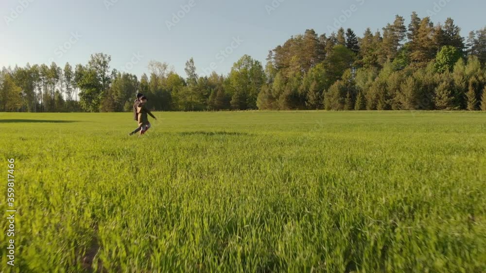 Drone flyes towards happy couple walking on meadow on sunny day, park