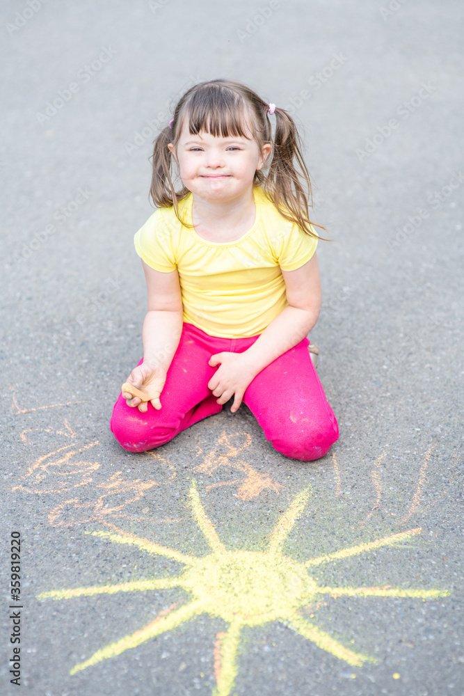 Smiling girl with syndrome down draws the sun with chalk on the asphalt Smiling girl with syndrome down draws the sun with chalk on the asphalt
