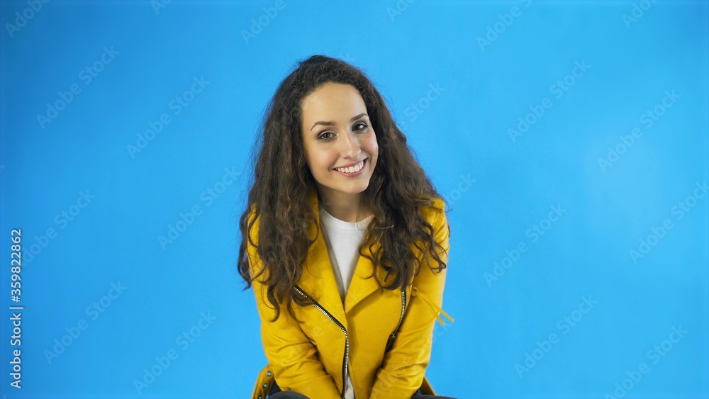 Happy Pretty Woman in yellow jacket Winking Eye in Studio with blue Background. Happy Pretty Woman in yellow jacket Winking Eye in Studio with blue Background.