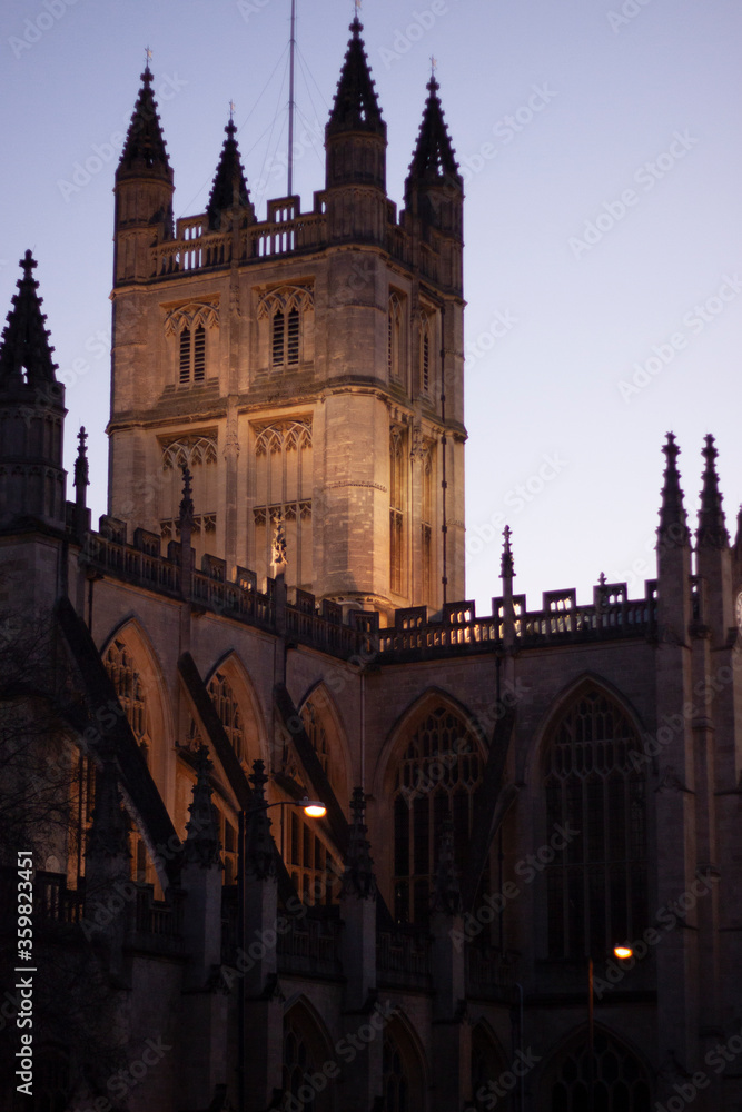 Close up image of the tower of the historic Bath Abbey against clear night sky. Artificial lights illuminate the tower and give it a warm look.
