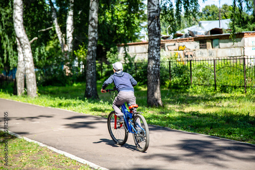 boy rides a bicycle on a park path, rear view