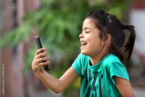 A young indian girl excited watching mobile phone. Happiness in mobile. Joyful baby girl. Excited baby girl. Playing with mobile.