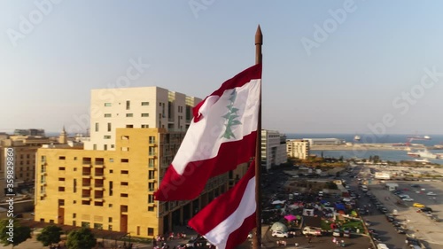 Beirut, Lebanon 2019: sunset turn around slow motion drone shot with Lebanese flag in foreground, mosque, church and sun flaring in the background during the Lebanese revolution photo