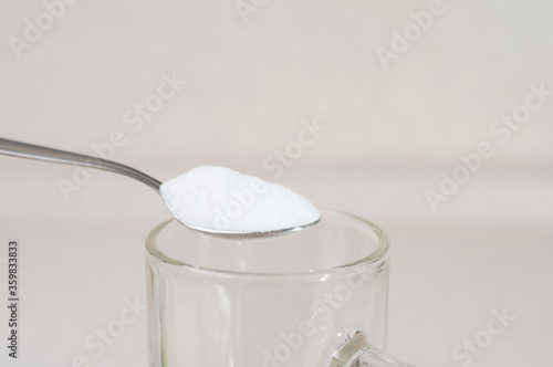 White tasteless creatine powder on a teaspoon over a transparent glass. Sports supplements and nutrition for recovery and progress