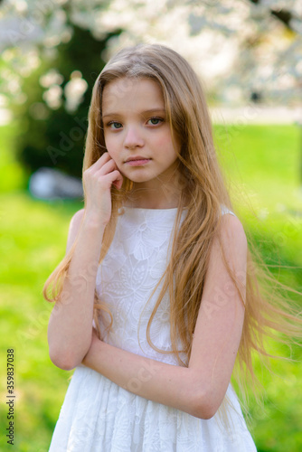 Beautiful blue-eyed girl with long blond hair in a white dress walking in the flower garden. summer bright, emotional photo.