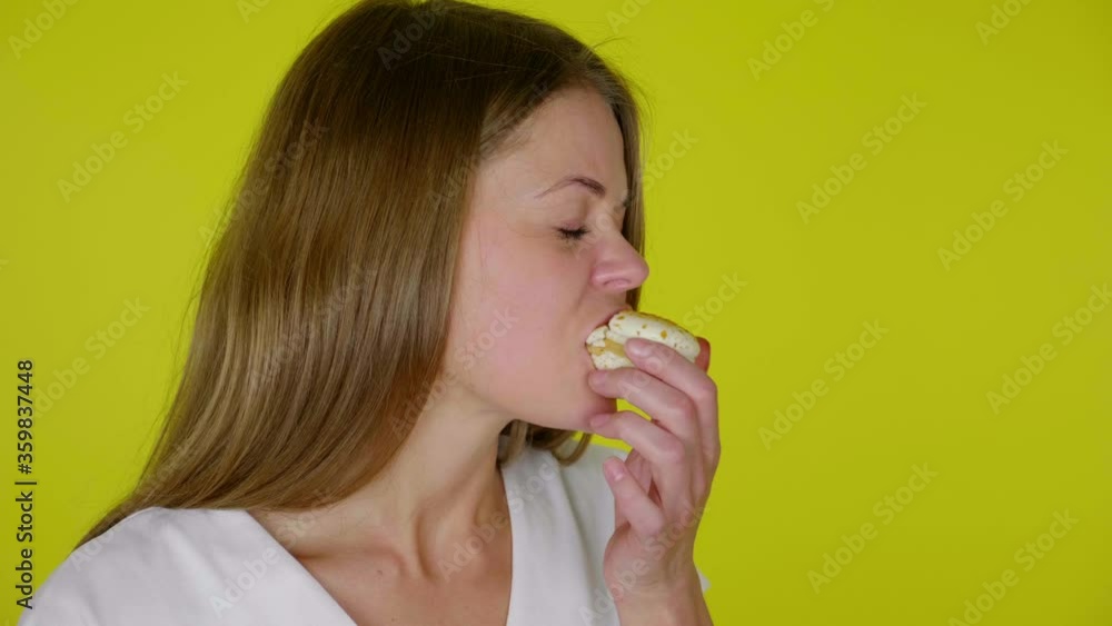 Close up woman in a white T-shirt bites a white macaroon, eats and is unhappy with the taste on a yellow background with copy space. Place for text or product. 4K slow motion footage Close up woman in a white T-shirt bites a white macaroon, eats and is unhappy with the taste on a yellow background with copy space. Place for text or product. 4K slow motion footage