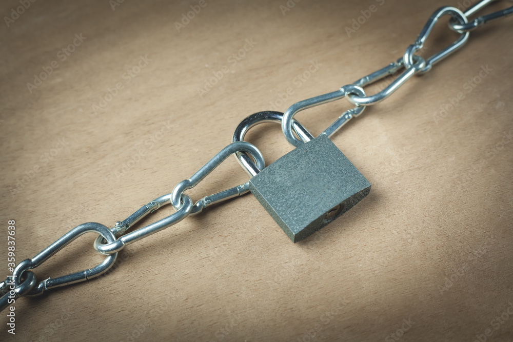 Padlock with a steel chain on a wooden background. Padlock with a steel chain on a wooden background.