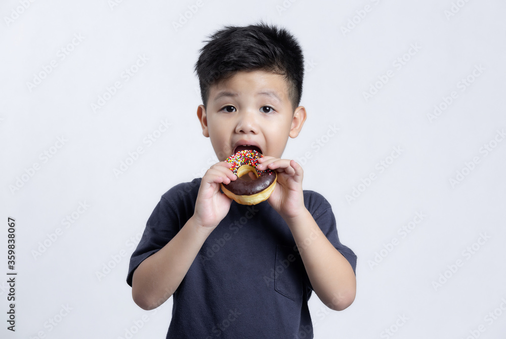 Little happy cute boy is eating donut on gray background. child is having fun with donut. Tasty food for kids Little happy cute boy is eating donut on gray background. child is having fun with donut. Tasty food for kids