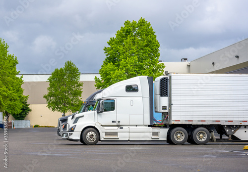 Big rig semi trucks with refrigerator semi trailer loading frozen cargo standing at warehouse dock gates
