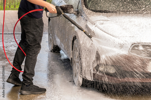 a man washes a brown car with a gun for washing high pressure cars