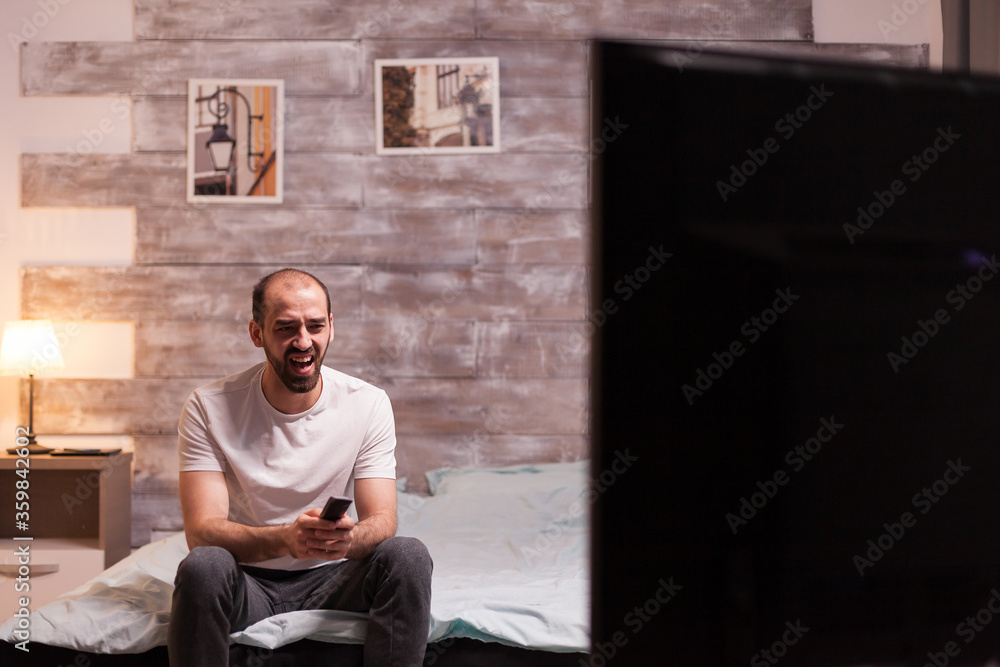 Man in pajamas laughing while watching a comedy on tv at night. Man in pajamas laughing while watching a comedy on tv at night.