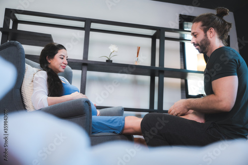 pregnant woman lies on a sofa. A man massage her feet. She is very pleased and she is well, concept of family at home © chokniti