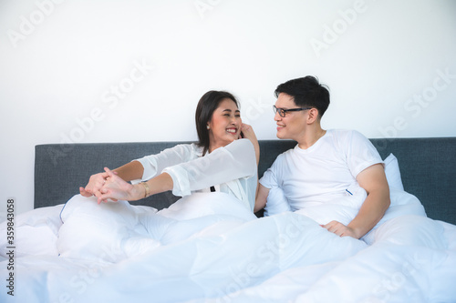 happy young couple wake up in bed and smiling raise arms in the morning, asian lovers on white bed
