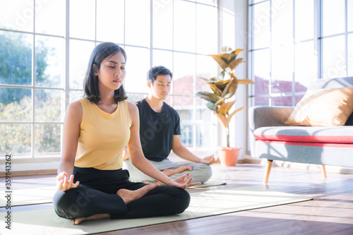 The Asian young couple yoga performer the meditating in lotus and cobra position at the cozy home in living room under the stay home situation