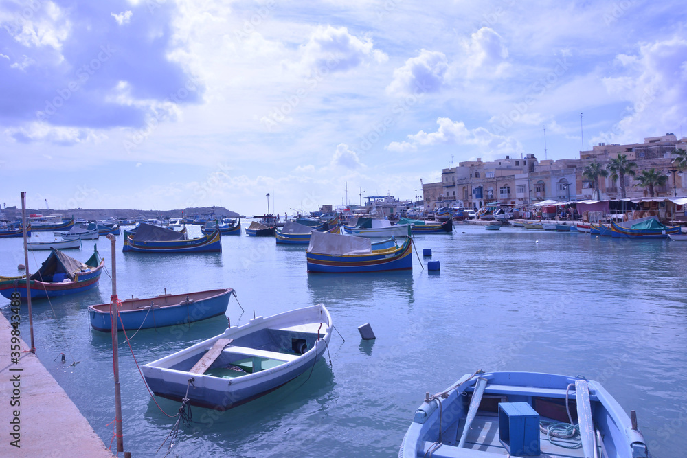 Multi-colored fishing boats rest in the sea bay against the background of a small old golden city and a blue sky.