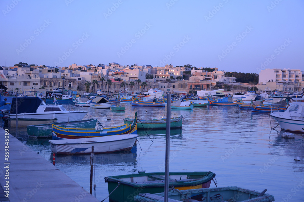 Multi-colored fishing boats rest in the sea bay against the background of a small old golden city and a blue cloudless sky.