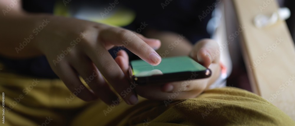 A girl touching on mock-up smartphone while sitting cross legged beside window in living room A girl touching on mock-up smartphone while sitting cross legged beside window in living room
