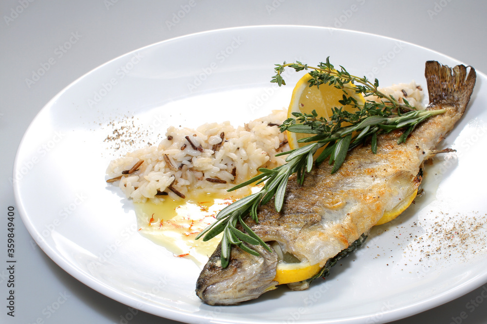 Baked trout with lemon, rosemary and wild rice on a white plate Baked trout with lemon, rosemary and wild rice on a white plate