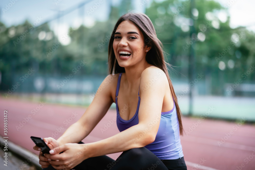 Beautiful woman resting from working out. Young athlete woman sitting on bench and using the phone after training.	