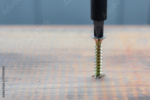 the metal screw crewed into the wooden board surface with screwdriver. home or workshop repair concept