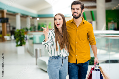 Husband look unbelievable discount. Two people married couple go walk free time in shopping center girl see incredible bargain point index finger indicate man hold many packages © deagreez