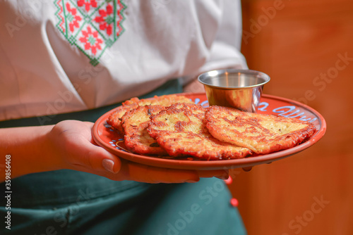 Potato pancakes dranik with sour cream, traditional Ukrainian dish. Waiter in traditional uniform serving dranyki. photo