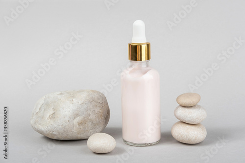 Pink anti-aging collagen  facial serum in transparent glass bottle with gold pipette and natural stones on grey background. Natural Organic Spa Cosmetic Beauty Concept. Front view