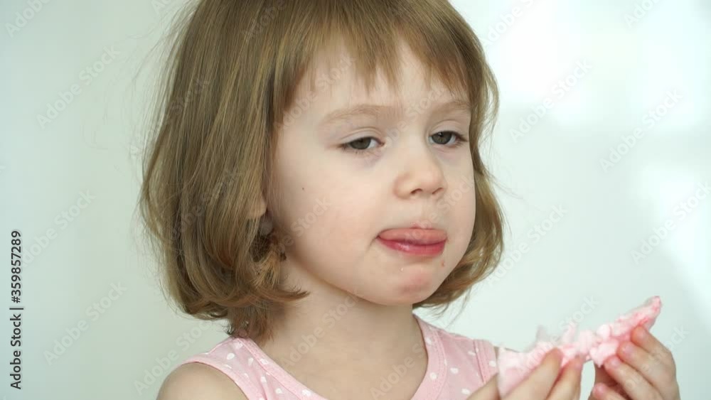 Close up of little funny 3 years old child girl eats pink cotton candy looks at camera, smiles and laughs. Sweets concept Close up of little funny 3 years old child girl eats pink cotton candy looks at camera, smiles and laughs. Sweets concept