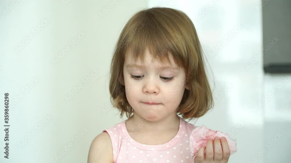 Portrait of little funny 3 years old child girl eats with appetite pink cotton candy, looks at camera, smiles and laughs. Close-up. Sweet kids food Portrait of little funny 3 years old child girl eats with appetite pink cotton candy, looks at camera, smiles and laughs. Close-up. Sweet kids food