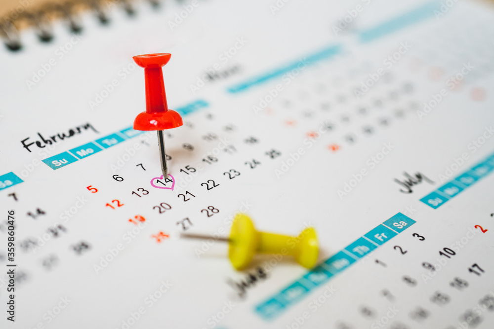 red push pin marked on 14th of February with red heart shape on white calendar red push pin marked on 14th of February with red heart shape on white calendar
