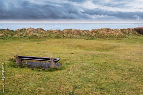 Empty wooden bench by the ocean, with beautiful relaxing view. Rosses point, county Sligo, Ireland, Nobody, Blud cloudy sky,
