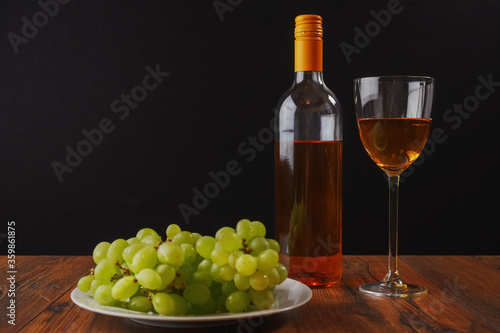 Still life image. White wine and cluster of fresh juicy grapes on a white plate and glass of wine, Black background. Concept winery production.