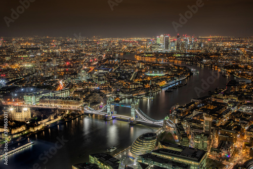 Aerial photograph of London city and Tower Bridge and the River Thames at night showing city lights leading to Canary Wharf, London England. 