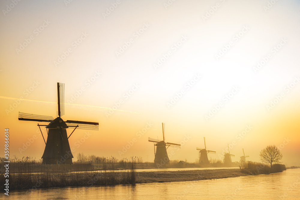 Alignement of five majestic windmills along a calm water canal at the gradient warm color sunrise in Alblasserdam, Netherlands