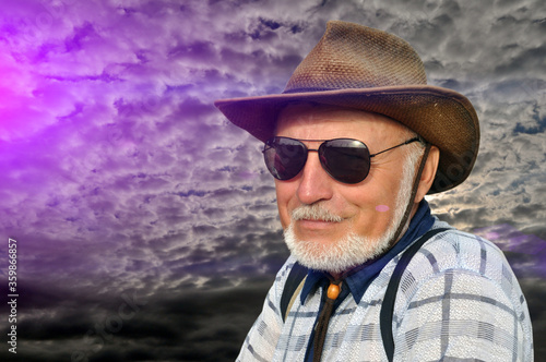 Portrait of a man in hats and black sunglasses with a beard. Smiling and looking while relaxing in nature during sunset. © Александр Байдук