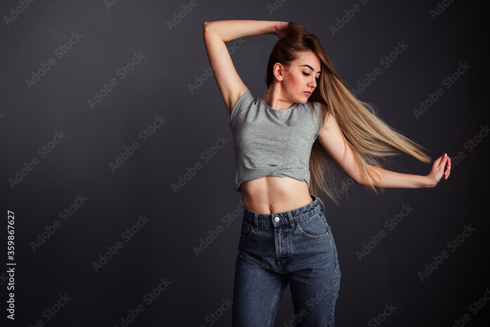 A thin girl with blond long hair looks away and straightens her hair against a dark wall A thin girl with blond long hair looks away and straightens her hair against a dark wall