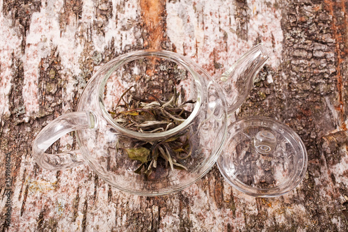 Bai Mu Dan (White Peony) dry white tea in the transparent teapot on the birch bark background photo