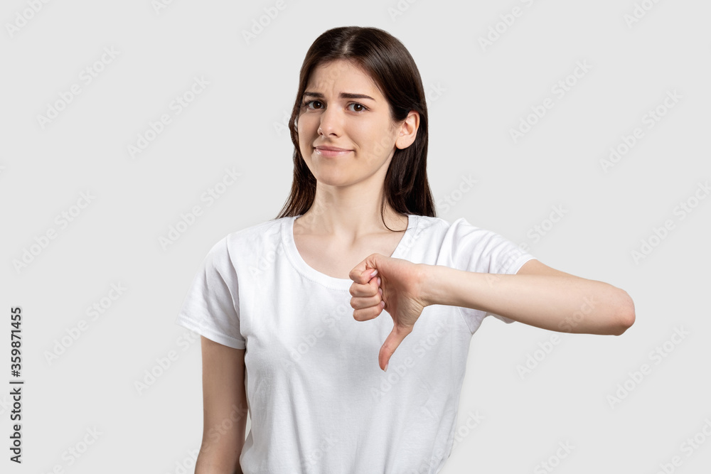 Dislike gesture. Bad idea. Disappointed woman showing thumb down isolated on light background. Dislike gesture. Bad idea. Disappointed woman showing thumb down isolated on light background.
