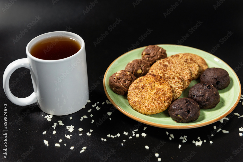 Tasty chocolate cookies with a tea cup on the black background Tasty chocolate cookies with a tea cup on the black background