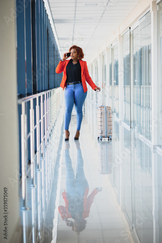 Full body profile portrait of happy female traveler walking with suitcase bag and cellphone