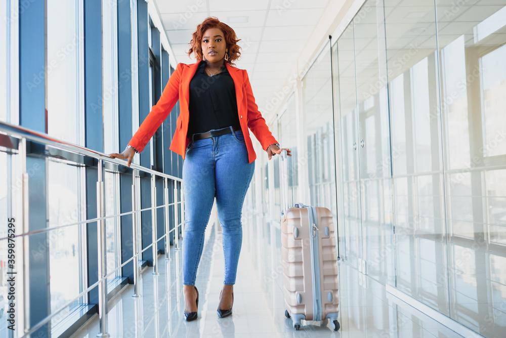 black woman in the moving walkway at the airport with a pink suitcase.