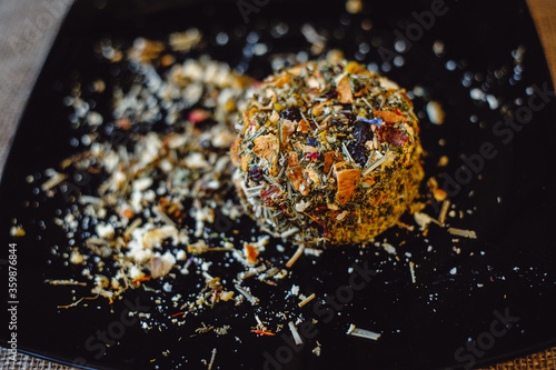 Bild auf Leinwand The round head of the French spicy cheese Boulette d'Avesnes sprinkled with different herbs, lies on a black plate