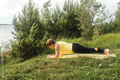 Senior woman making yoga near river in summer. Plank pose. photo