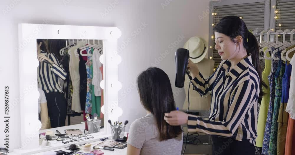 Great style. slow motion delighted pleasant woman model smiling while having hairstyle done in dressing room before show. lady fashion stylist talking and using hair dryer prepare in backstage Great style. slow motion delighted pleasant woman model smiling while having hairstyle done in dressing room before show. lady fashion stylist talking and using hair dryer prepare in backstage