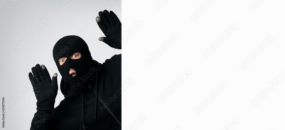 Masked thief with raised arms isolated on white wall Masked thief with raised arms isolated on white wall
