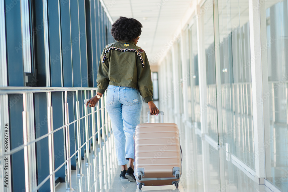 Young african american female passanger in casual clothes is in airport with baggage.
