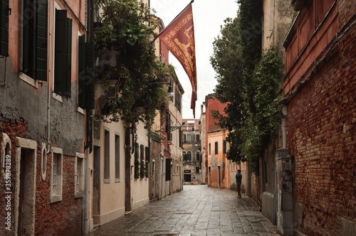 Venetian street with a hanging flag on the facade of an old house. Italy.