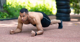 Core body workout. Shirtless black athlete doing elbow plank on asphalt road at summer park