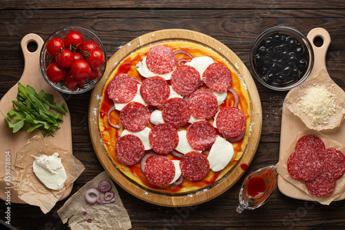 Process of making homemade pizza with mozzarella olives and salami, top view photo