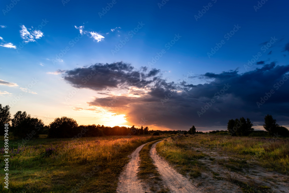 Road in the field among green grass and beautiful sky in the evening.